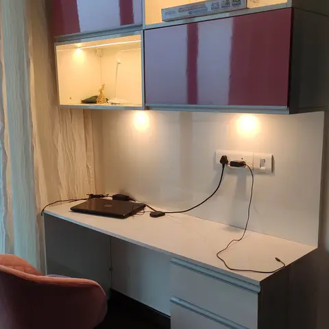 Built-in study desk unit with backlit open display cubbies and glossy maroon overhead cabinets, a white work desk with drawer storage below