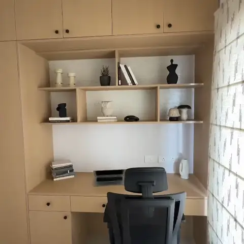 Built-in study desk with an open display shelf styled with books and small figurines, wood-veneer overhead cabinets