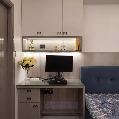 Built-in study nook in greige laminate with black M-shaped handles, a glass-topped desk running up to a blue tufted daybed