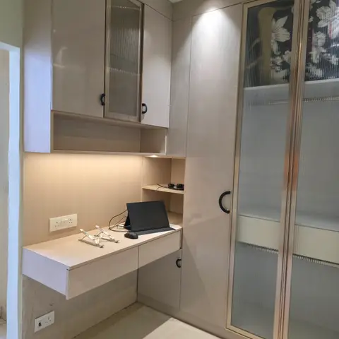 Built-in study nook with a floating desk, backlit open shelving and a fluted-glass overhead cabinet, beside a tall wardrobe with mirrored floral-glass shutters.