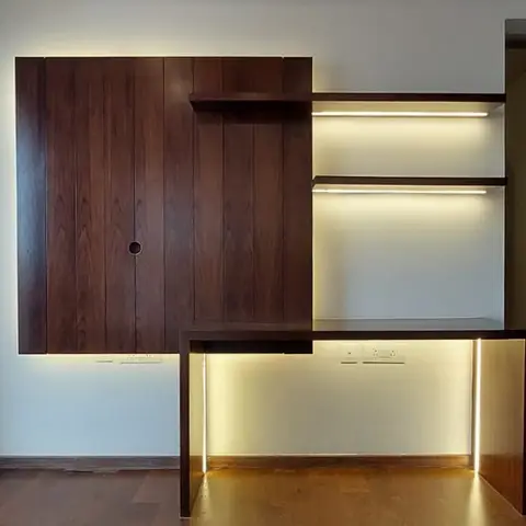Built-in study nook with a dark wood-veneer panelled wall and cabinet, backlit floating shelves, and a matching wood desk edged with a warm LED strip.