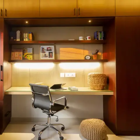 Built-in study nook with warm wood cabinetry, open shelving styled with books and framed photos, under-shelf lighting, and a black mesh office chair