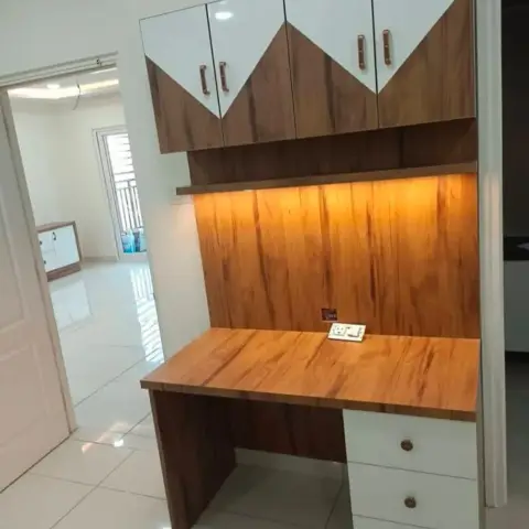 Built-in wood-laminate study desk with overhead diamond-pattern cabinets and warm profile lighting above the worktop.