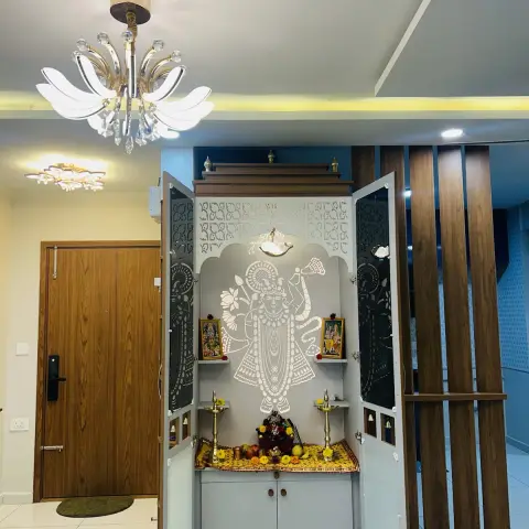 Built pooja mandir photographed with its jaali shutters open: a white Shrinathji figure etched on the grey back panel, brass diyas and marigold on the counter