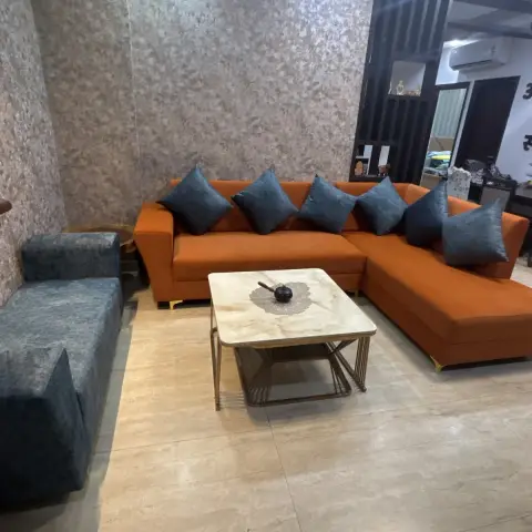 Burnt-orange L-sectional stacked with slate-blue cushions against a mottled metallic wallpaper wall, a black slat screen opening to the dining beyond.