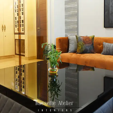 Burnt-orange tufted sofa with a black quilted glass coffee table, facing a gallery wall, with entrance wardrobes visible beyond a stone pillar.