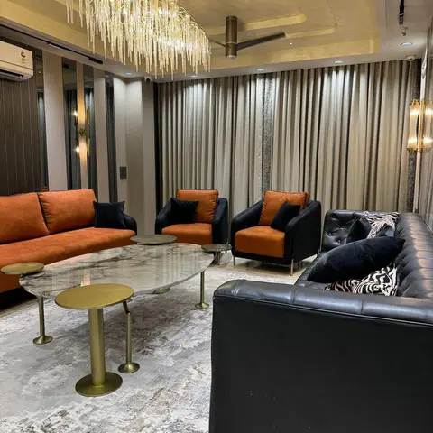 Burnt-orange velvet sofa and armchairs paired with a black tufted leather sofa around an oval marble coffee table with brass legs