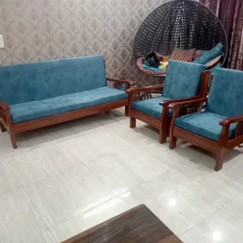 Carved wood-frame sofa set upholstered in teal velvet, paired with a black wicker hanging egg chair against damask wallpaper.