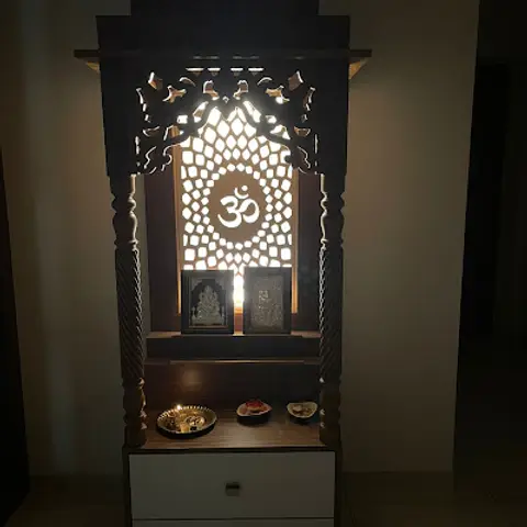 Carved wood pooja unit with a backlit Om jaali panel above white drawer storage.