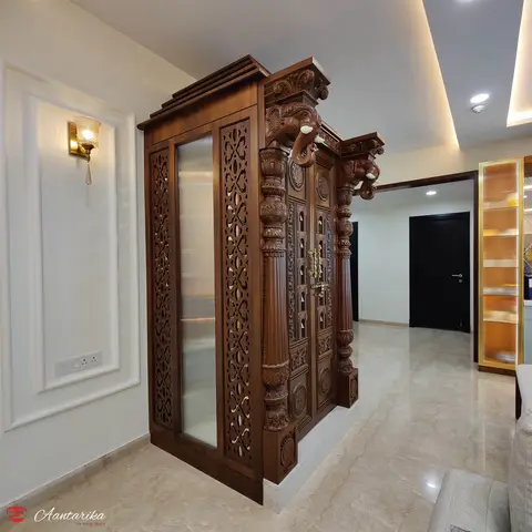 Carved wood pooja unit with elephant-head brackets, jaali screen side panels, fluted pillars, and a gold latch door, set in a marble-floored foyer.