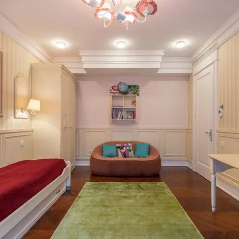 Child's bedroom with a red-upholstered single bed, green rug, and a wall-mounted shelf styled with books and a globe