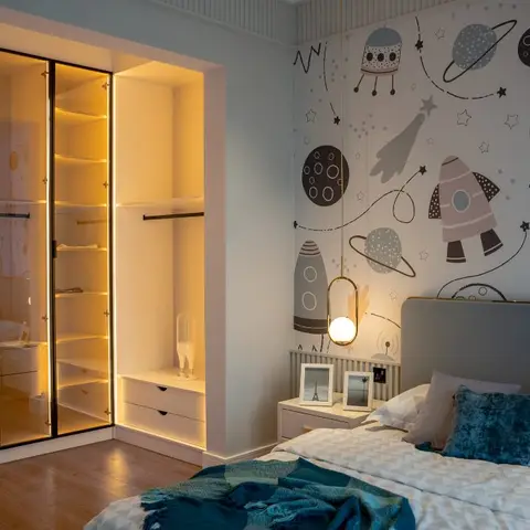 Child's bedroom with a space-and-rocket themed wallpaper behind the bed and a backlit glass-front wardrobe with a walk-in dressing nook.