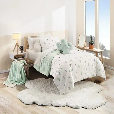 Child's bedroom with cactus-print bedding, a plush cactus pillow and a cloud-shaped white fluffy rug beside a simple wood slat bed frame