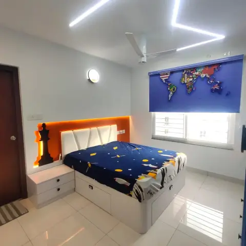 Child's room with a rocket-print duvet on a white storage bed, an orange-backlit chess-king cutout beside the cushioned headboard and a flag world-map roller