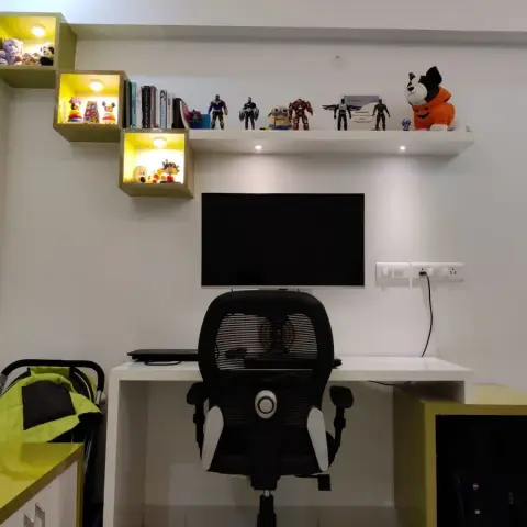 Child's study corner with a white L-desk and mesh gaming chair under a wall-mounted screen