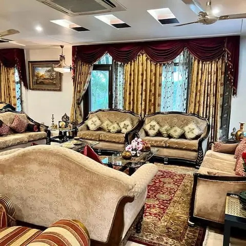 Classic carved-wood sofa set upholstered in cream with maroon-and-gold swag curtains and a floral patterned rug