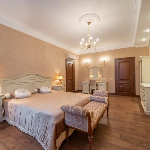 Classic master bedroom with damask wallpaper, a crystal chandelier, a vanity dresser and a cushioned bench at the foot of the bed