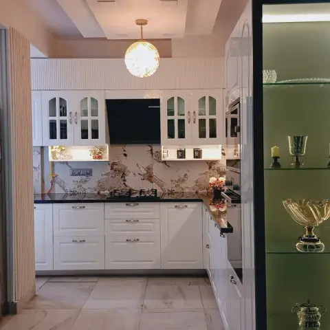 Classic white kitchen with glass-panelled upper cabinets, a dramatic veined marble backsplash and black granite counters, a globe pendant light