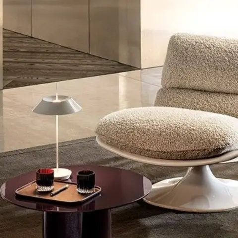 Close styling shot of a boucle swivel lounge chair on a white tulip base beside a small round side table with a table lamp