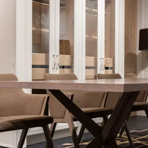 Close-up of a wood dining table with X-cross legs surrounded by brown upholstered armchairs