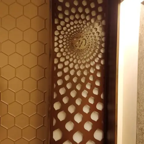 Close-up of a wood-framed pooja niche with a laser-cut jaali screen featuring a radiating dot pattern and a central Om symbol