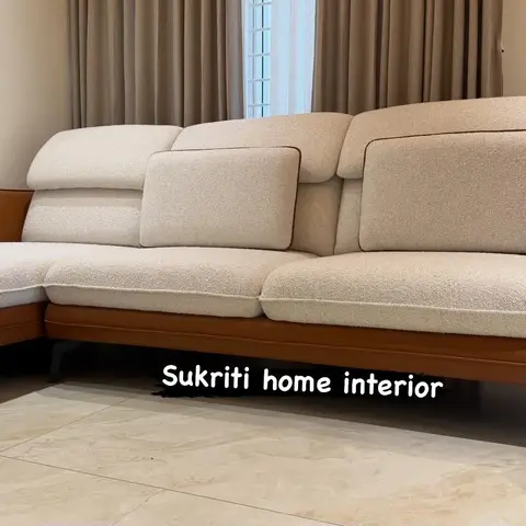 Close view of a tan leather and cream bouclé L-shaped sofa against a curtained window, on beige marble-look flooring.