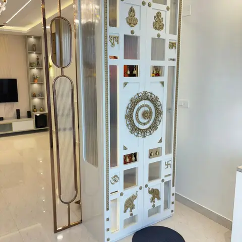 Closed white lacquered pooja cabinet with brass Ganesh and lotus motifs and fluted glass doors, beside a full-length reeded-glass mirror divider