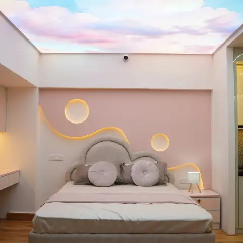 Cloud-shaped upholstered headboard against a blush wall cut with a backlit wavy groove and two glowing discs, under a printed pastel sky ceiling.