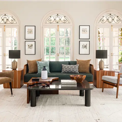 Colonial-arched living room with a dark green velvet sofa, black stone coffee table and mid-century armchairs on a patterned rug