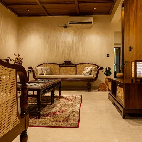 Colonial-style living room with a cane-backed wooden settee, a coffered wood ceiling, and a patterned red-bordered rug over marble flooring.