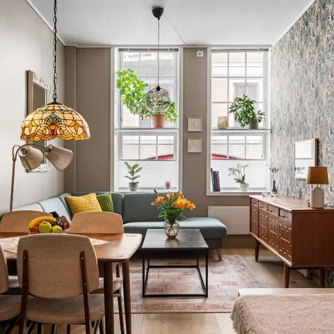 Combined living-dining room with a vintage wooden dining set, a teal corner sofa and a botanical-print wallpaper accent wall