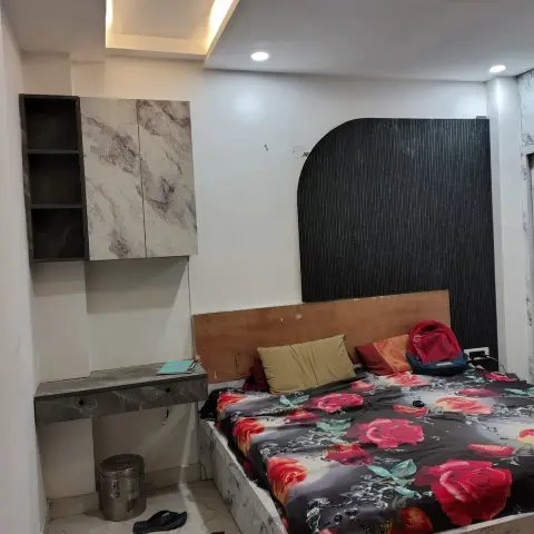 Compact bedroom near handover: an arched black fluted panel sits behind a bare plywood headboard on a marble-laminate platform bed