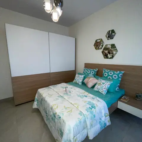 Compact bedroom shot from the doorway: a floor-to-ceiling sliding wardrobe in white over walnut laminate, teal floral bedding