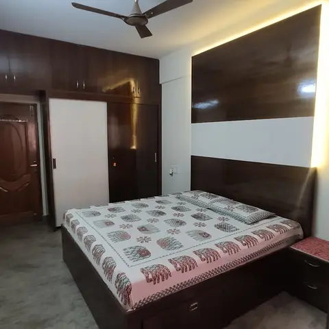 Compact bedroom where a dark walnut-laminate storage bed sits against a backlit headboard panel
