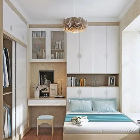 Compact bedroom where a light-oak storage bed sits under a bank of white overhead lofts and an open book shelf