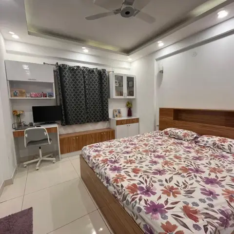 Compact bedroom where a teak-laminate headboard with a built-in display ledge meets a white-and-teak study desk under a gloss wall cabinet