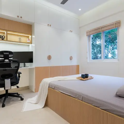 Compact bedroom with a built-in study nook under a lit open-shelf unit, a white-and-wood wardrobe wall, and a low platform bed with a wood base.