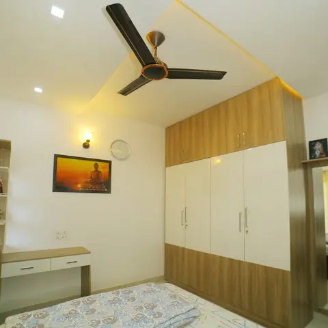 Compact bedroom with a four-shutter oak-and-white wardrobe with loft boxes lit by a cove above it