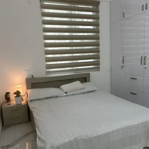 Compact bedroom with a light-oak laminate bed and matching two-drawer nightstand set under a beige zebra blind