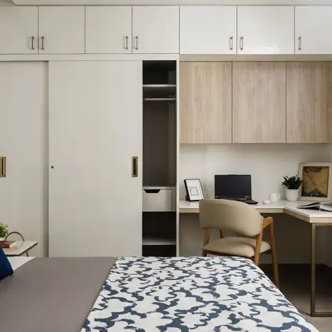 Compact bedroom with a navy upholstered headboard and blue-print quilt facing an ivory sliding wardrobe with loft units