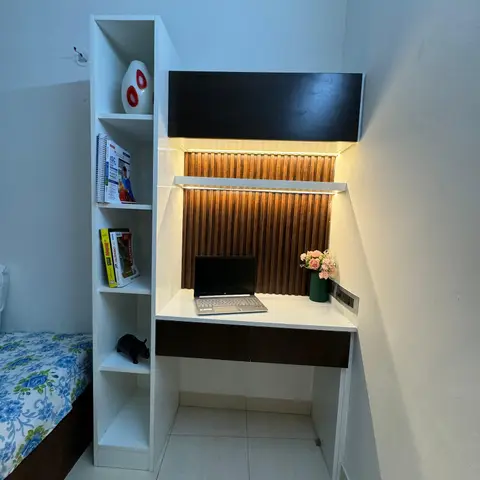 Compact built-in study nook with fluted wood panelling, backlit profile lighting, an open bookshelf of school textbooks and a laptop on the desk
