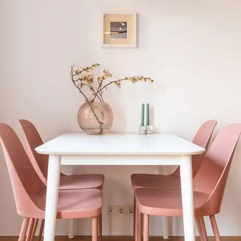 Compact four-seat dining nook with dusty-pink chairs against a plain wall styled with a single framed print.