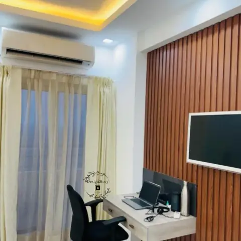 Compact home office nook with a wall-mounted study desk against a vertical wood-slat TV panel, sheer curtains, and a cove-lit ceiling with a split AC unit