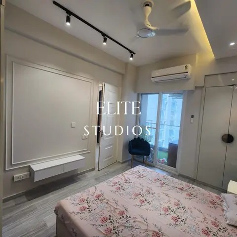 Compact Indian bedroom with a single large white moulding frame on the TV wall above a slim floating console, black track spots and a ceiling fan