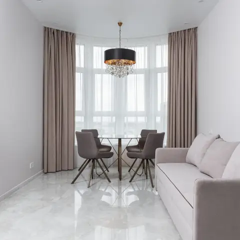 Compact living-dining room with a round glass dining table under a statement black drum chandelier, a blush sofa