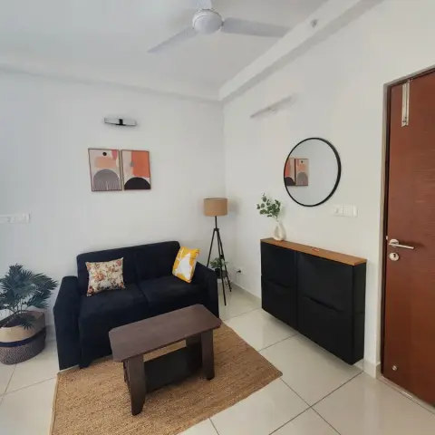Compact living room by the flat's teak main door, with a navy two-seater and a dark wood coffee table on a jute rug