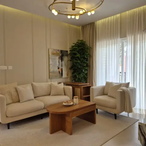 Compact living room in oatmeal fabric — three-seater and matching armchair with a throw, around a rounded teak coffee table on a jute rug