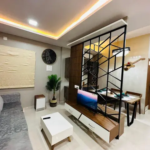 Compact living room where a black geometric MS screen on a walnut ledge splits the sofa and TV run from a four-seat dining table under a black drum chandelier.