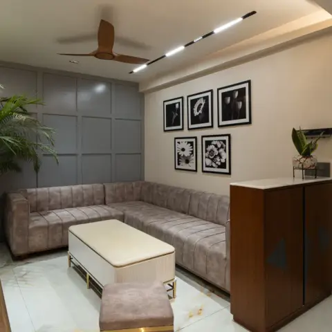Compact living room where a grey suede L-sofa runs along a grid-moulded grey wall, five black-and-white botanical prints hang in a two-row grid