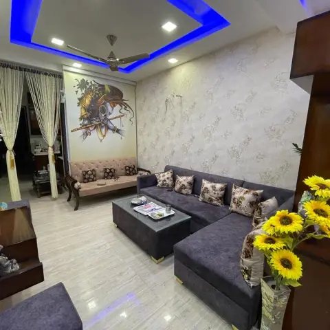 Compact living room with a grey L-shaped velvet sofa and a matching upholstered ottoman table against beige floral wallpaper